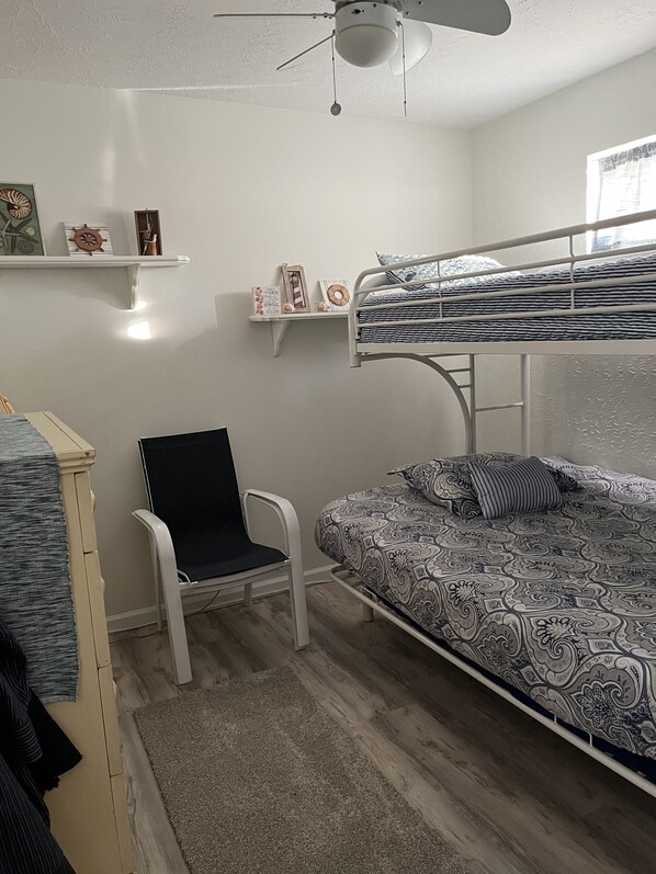 A bedroom with a bunk bed, a desk, a chair, and a ceiling fan.