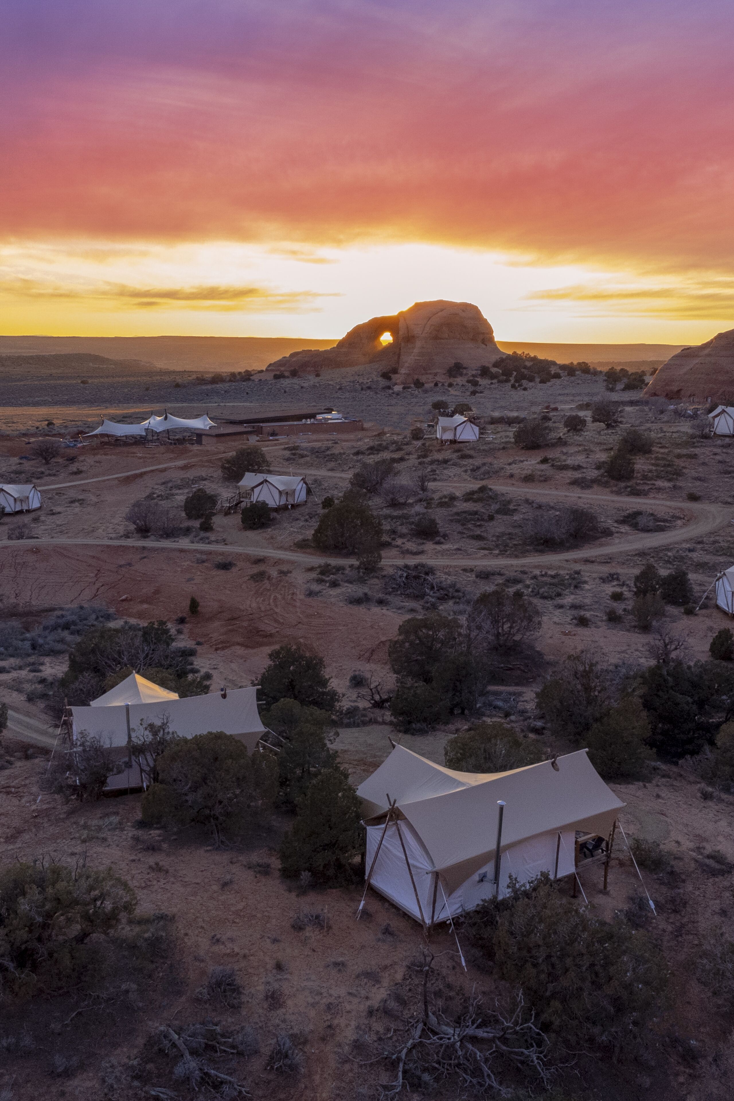 A desert landscape with several tents and a prominent rock formation in the background.