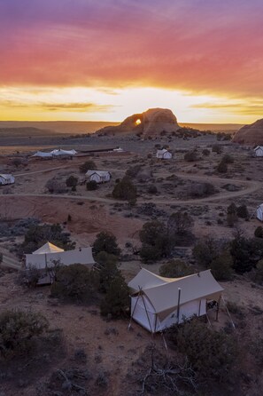A desert landscape with several tents and a prominent rock formation in the background.