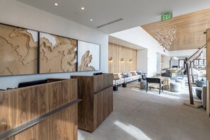 A modern reception area with wooden reception desks, a large wall-mounted artwork, and a staircase leading to upper floors.