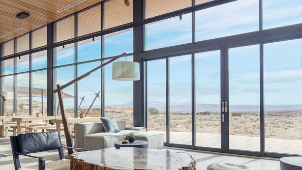A spacious interior with large windows, a wooden ceiling, and a central round table surrounded by seating. - ULUM Moab (La Sal)