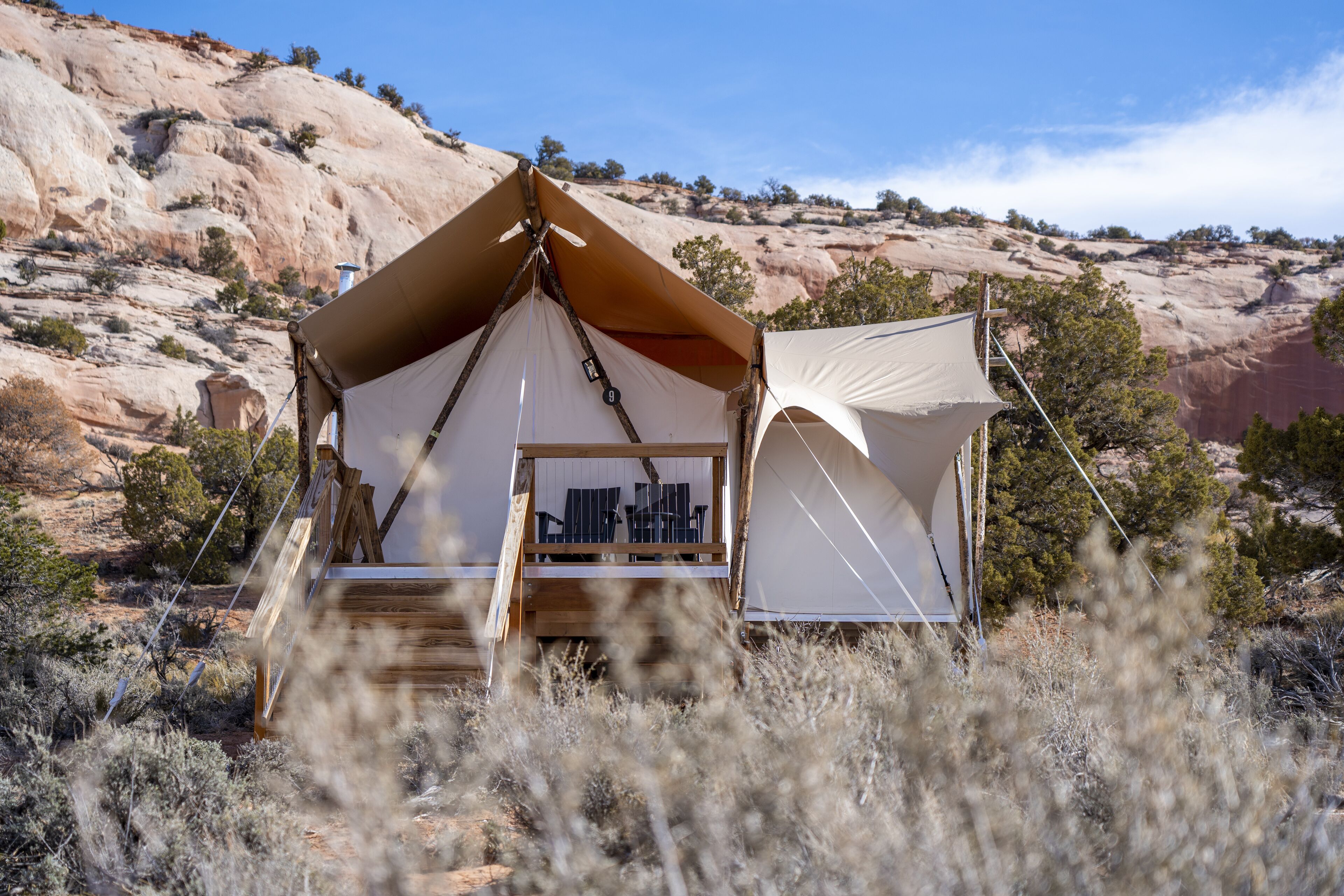 A tent with a wooden deck and a small table, surrounded by dry vegetation and a rocky landscape.