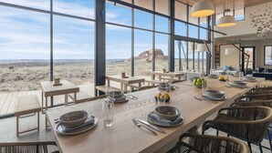 A dining area with a long table set for a meal, large windows offering a view of the desert landscape, and a modern interior design. - ULUM Moab (La Sal)