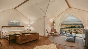 A tented room with a bed, a chair, a table, and a view of the landscape. - ULUM Moab (La Sal)