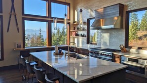 Une cuisine moderne dotée d’un grand îlot central, de tabourets de bar et offrant une vue sur les montagnes grâce à de grandes fenêtres.