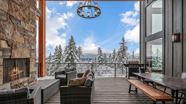 Une terrasse en bois, meublée de meubles en osier, avec une cheminée et une vue sur des arbres couverts de neige.