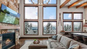 Un salon spacieux avec une cheminée, de grandes fenêtres offrant une vue sur le paysage enneigé et un coin salon confortable.