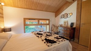 A bedroom with a wooden ceiling, a large bed with a cowhide blanket, a dresser, and a window with a view of greenery. - Chalet Gaïla spacious chalet in Les Allues next to the gondola (Meribel Les Allues)
