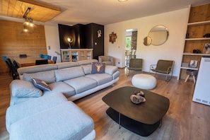 A modern living room with a sectional sofa, a round coffee table, and a dining area with a wooden table and chairs.