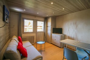 Een kamer met een bank, een klein rond tafeltje, een televisie, een bureau met toetsenbord en een stoel.