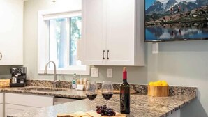 A kitchen with granite countertops, a wine bottle, glasses, and a painting of a mountain landscape.