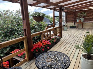 A wooden deck with a pergola, potted plants, and a round table with a decorative metal top.