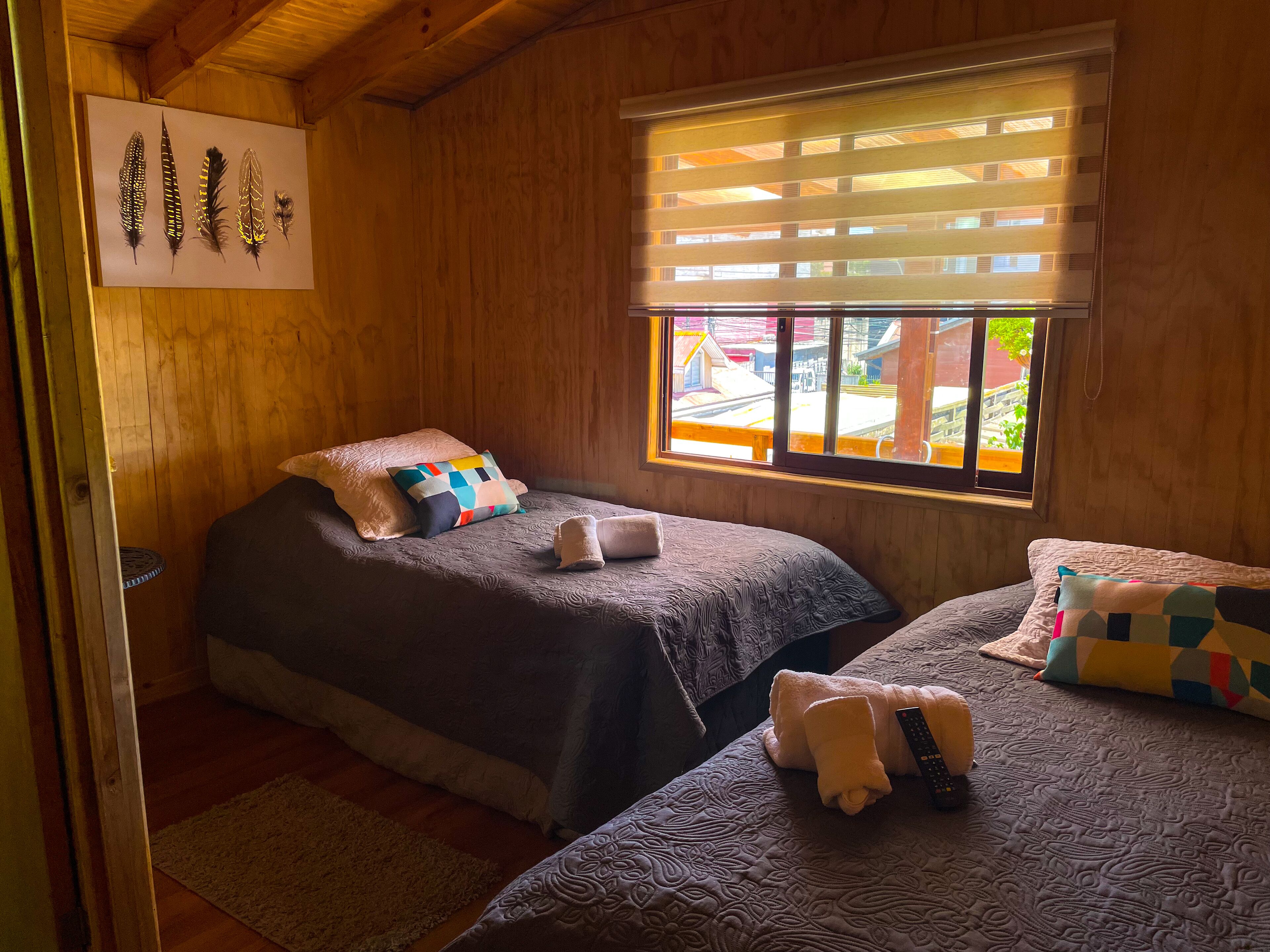 Una habitación acogedora con dos camas, una ventana con persianas, techo de madera y un cuadro colgado en la pared.