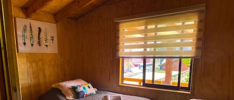 Una habitación acogedora con dos camas, una ventana con persianas, techo de madera y un cuadro colgado en la pared.