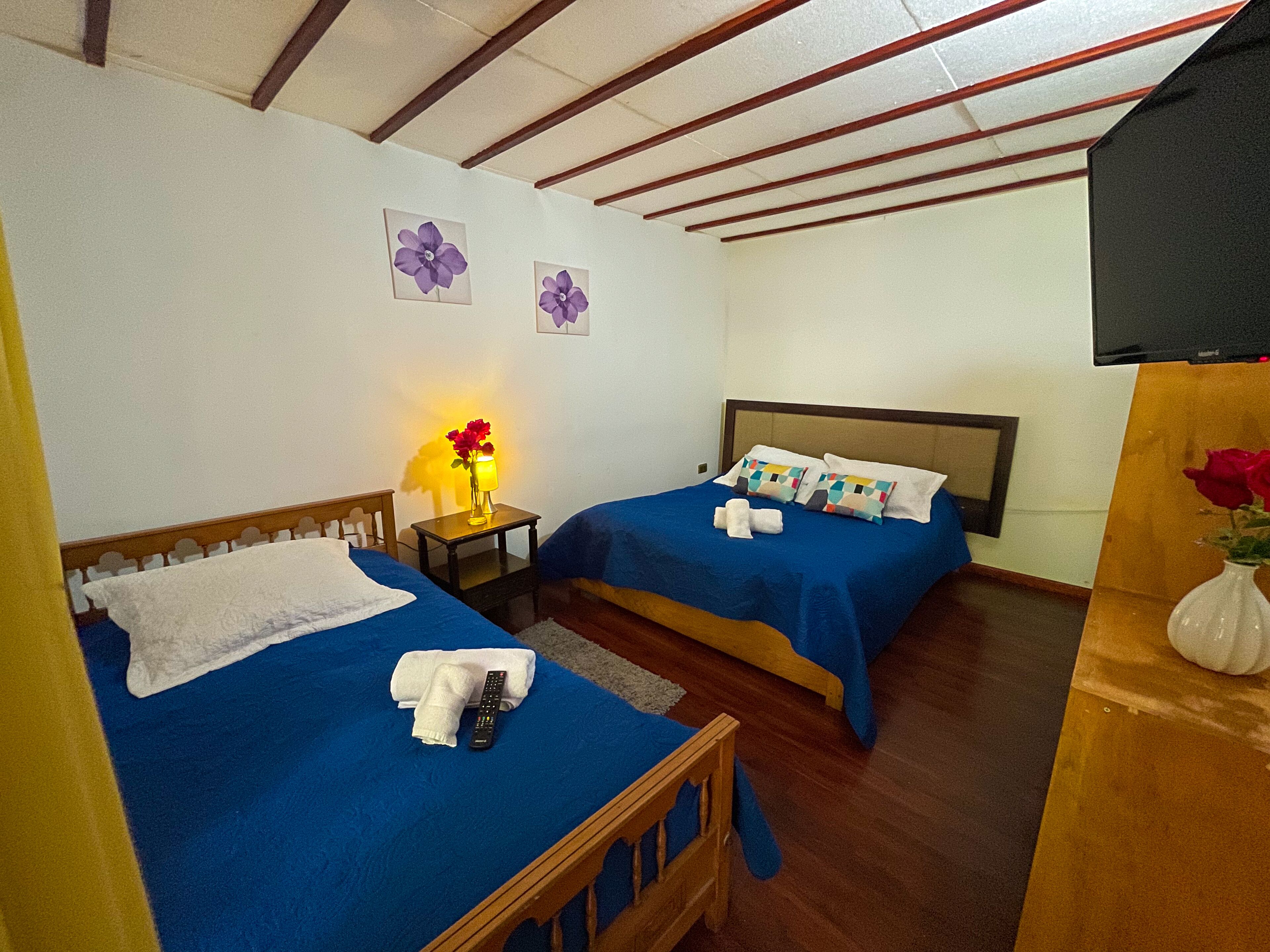 A hotel room with two beds, a nightstand with a lamp, and a TV on the wall.