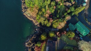 An aerial view of a coastal property with a house, a green-roofed building, and a small dock. - Whalers Guesthouse (Tofino)