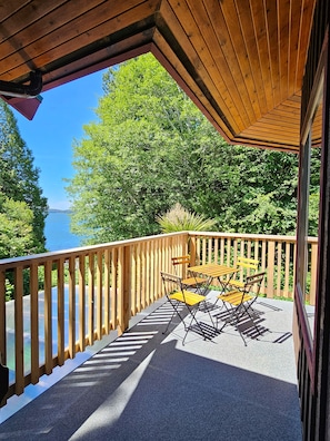 A wooden deck with a table and chairs, overlooking a body of water and surrounded by trees. - Whalers Guesthouse (Tofino)