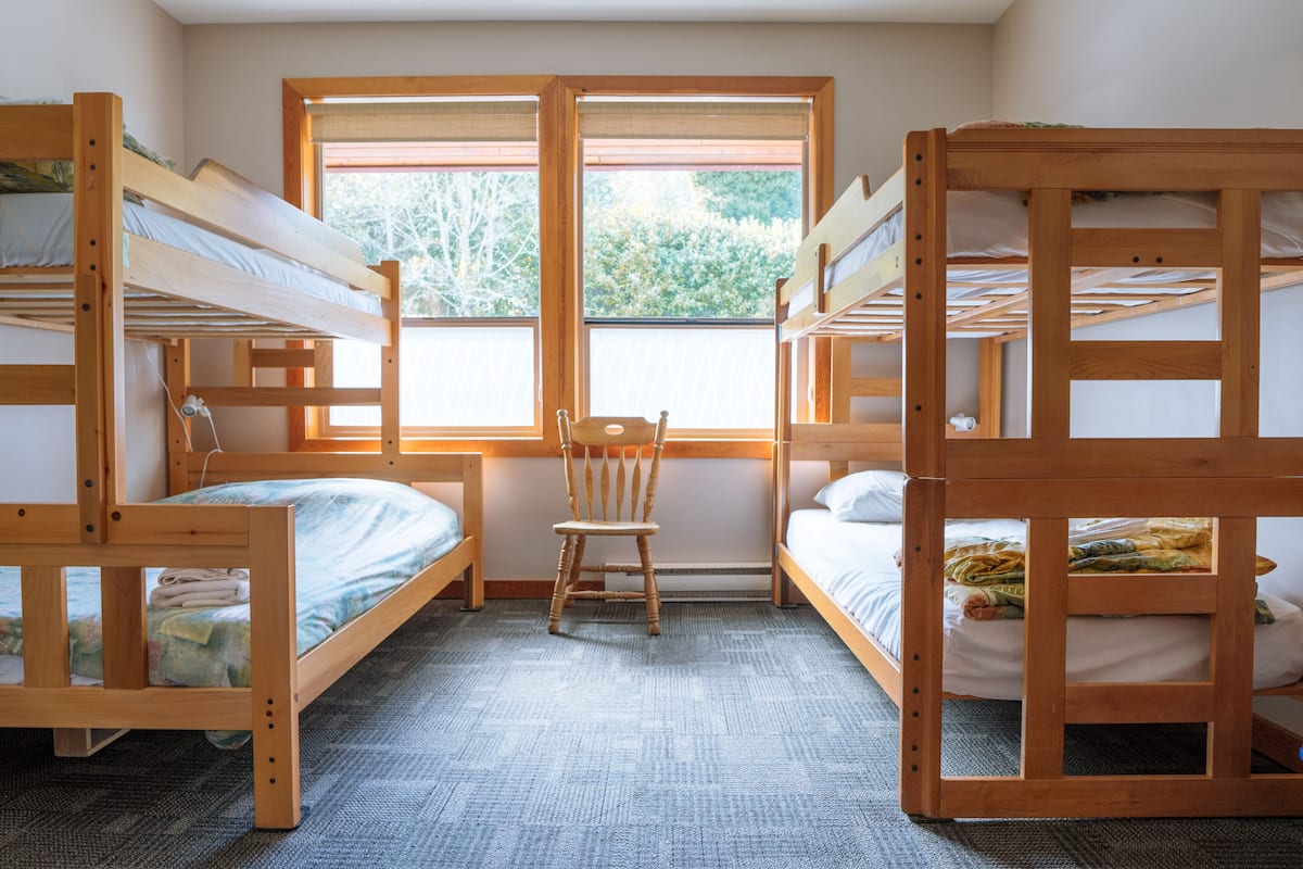 Een kamer met stapelbedden, een stoel en een raam met uitzicht op bomen.