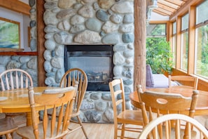 A stone fireplace with a black glass door, surrounded by wooden chairs and a table. - Whalers Guesthouse (Tofino)