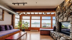 Amplia sala de estar con pared de piedra, vigas de madera y ventanas grandes con vistas a un lago.