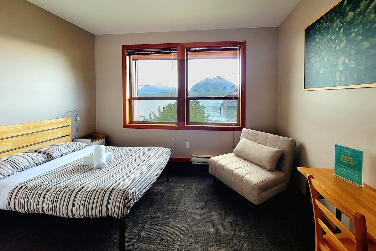 Een hotelkamer met een bed, een sofa, een bureau en een raam met uitzicht op bergen en water.