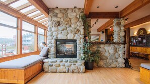 Una chimenea de piedra con un banco, vigas de madera y ventanas amplias.