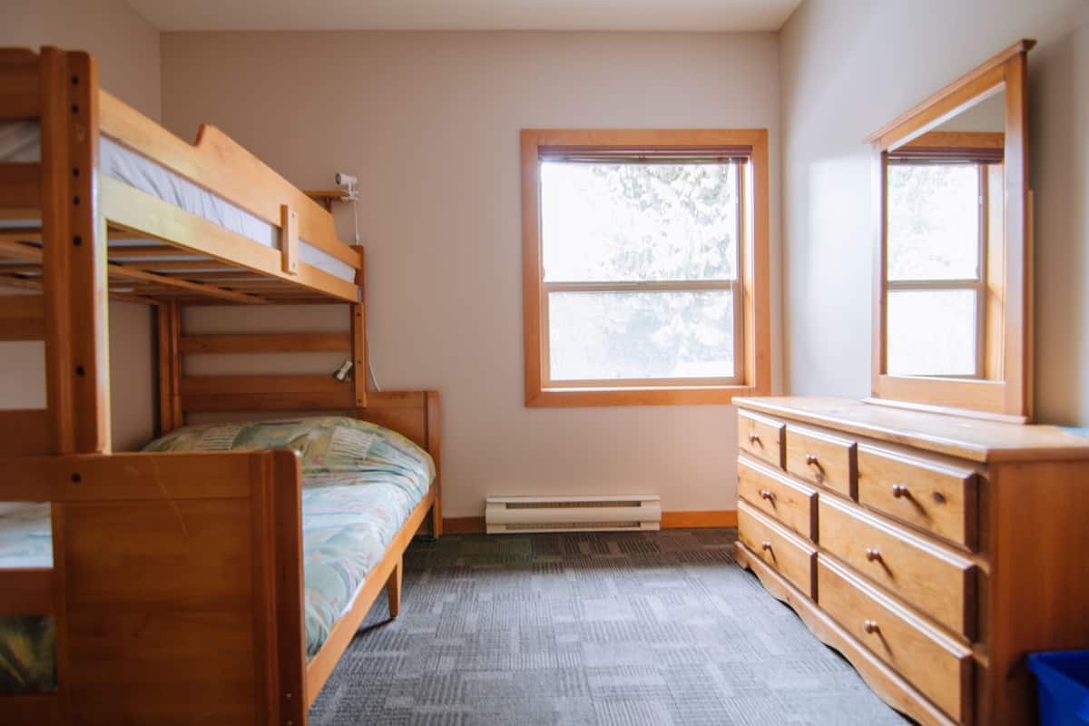 Een kamer met stapelbedden, een dressoir, een raam en een radiator.