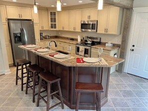 A kitchen with a central island, bar stools, a refrigerator, a microwave, and a stove. - Contemporary, Warm & Cozy mins to Saratoga (Ballston Spa)