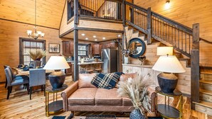 Ein gemütliches Blockhaushaus-Interieur mit einer Holztreppe, einem Essbereich und einem Wohnzimmer mit einer Couch und Lampen.