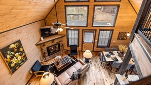 Ein gemütliches Blockhaus-Interieur mit Kamin, Sitzecke, Esstisch und großen Fenstern.