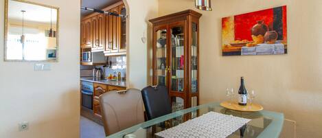 Un coin repas avec une table en verre, un meuble avec des portes en verre et un tableau accroché au mur.