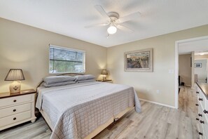 Ein Schlafzimmer mit Bett, Nachttischlampen, Deckenventilator, Fenster mit Jalousien und einem Bild an der Wand.