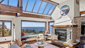 Un salón amplio con una chimenea grande, asientos cómodos y vistas al mar.