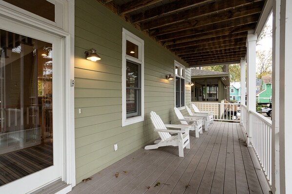 A porch with white Adirondack chairs, a wooden ceiling, and a green exterior wall.