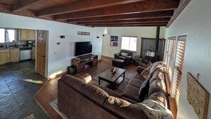 Ein geräumiges Wohnzimmer mit einem großen braunen Sofa, einem Flachbildfernseher und einer Holzbalkendecke.