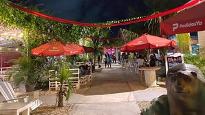 An outdoor dining area with red umbrellas, outdoor seating, and a sign for 'Benito's Sushi'.