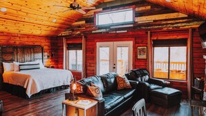 Interior de una cabaña de troncos con una cama, un sofá y una mesa de comedor.