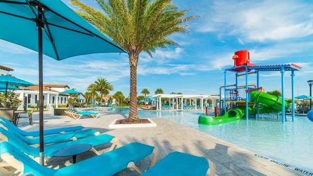 Area piscina con lettini, una palma e scivolo acquatico.