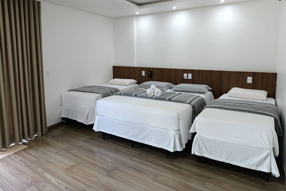 A hotel room with three beds, wooden flooring, and a ceiling light fixture.