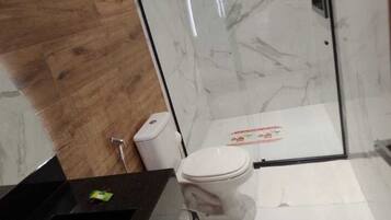 A bathroom with a wooden floor, a white toilet, a glass shower enclosure, and a black sink.