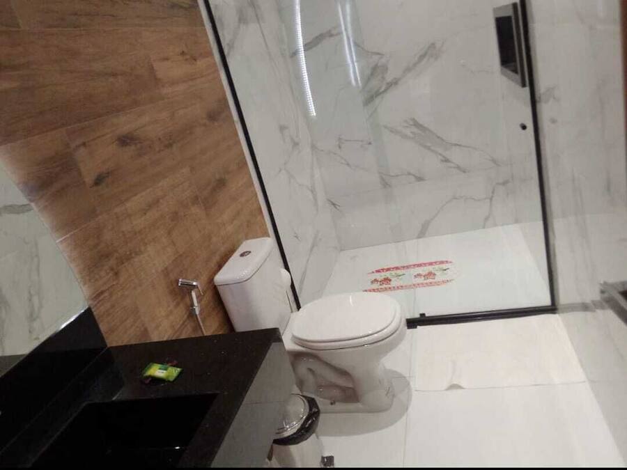 A bathroom with a wooden floor, a white toilet, a glass shower enclosure, and a black sink.