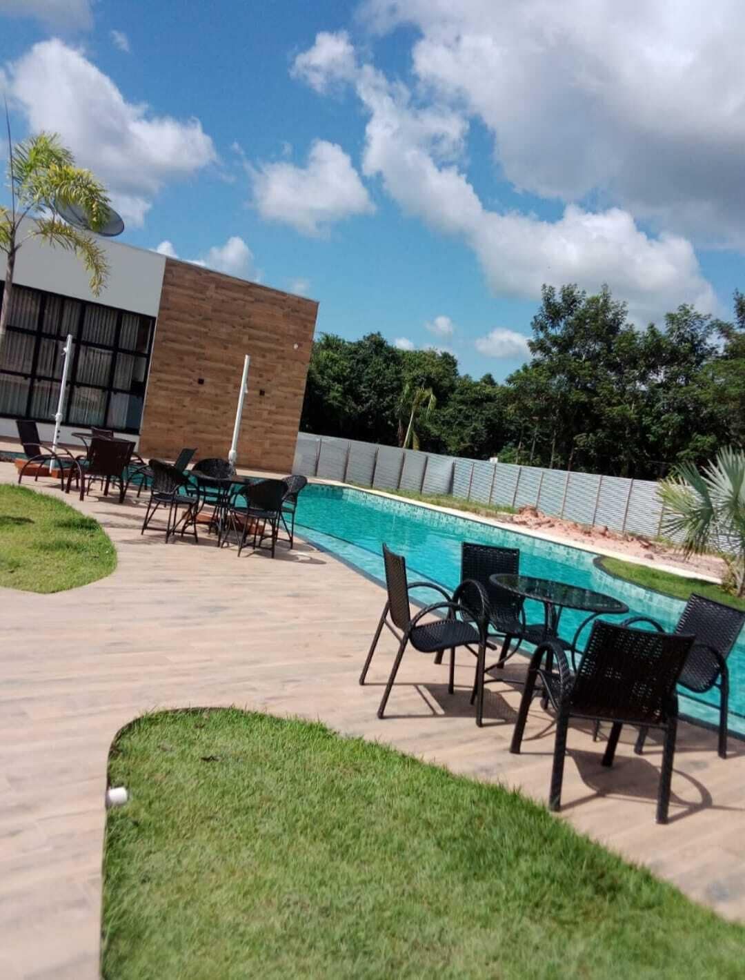 Un área de piscina moderna al aire libre con un edificio de madera, sillas de descanso y un cielo azul despejado.