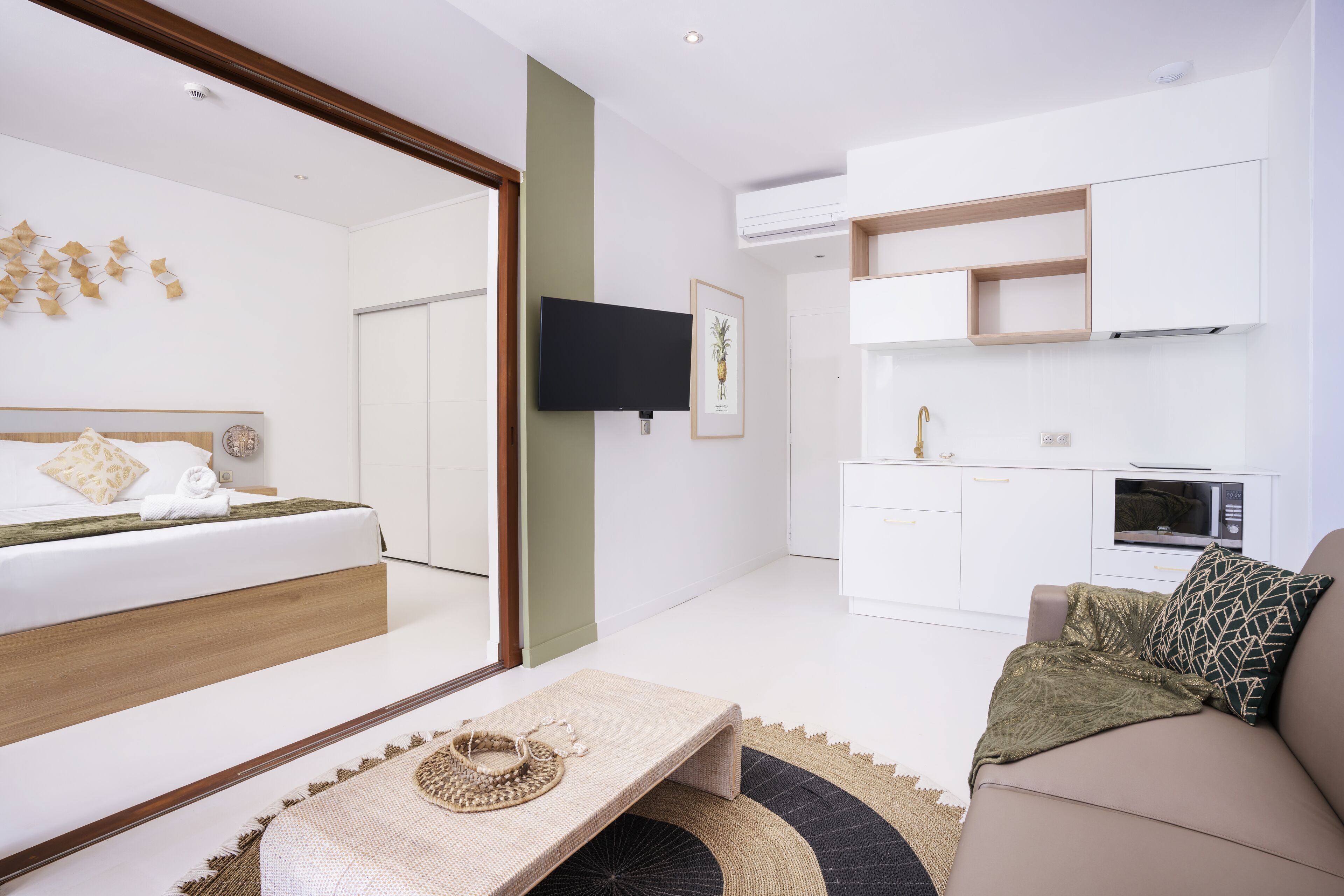 Una habitación de hotel moderna con una cama, un sofá, una mesita, un televisor y una kitchenette.