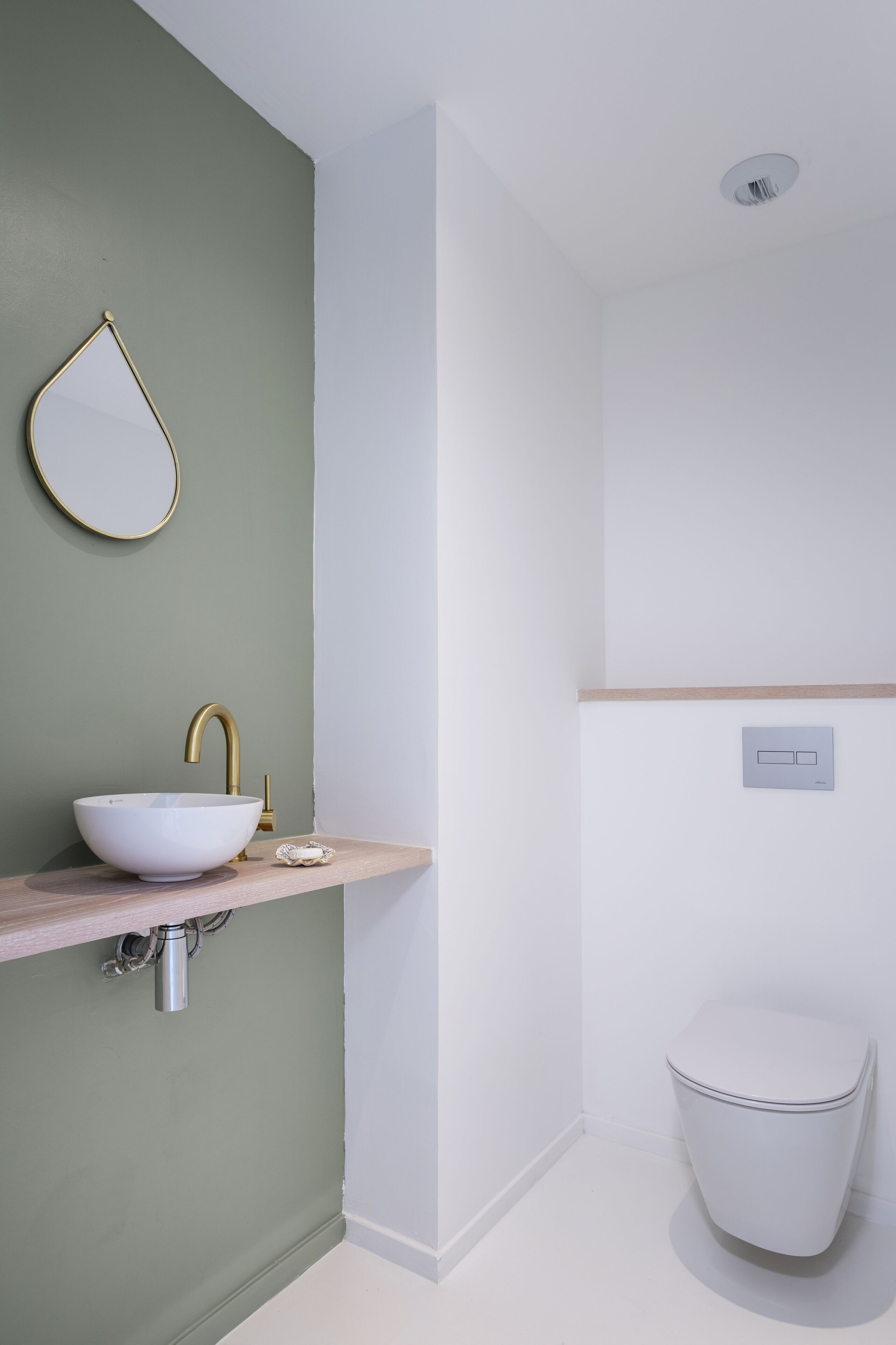 Un baño con lavamanos blanco, grifo dorado y un espejo redondo sobre una pared verde.