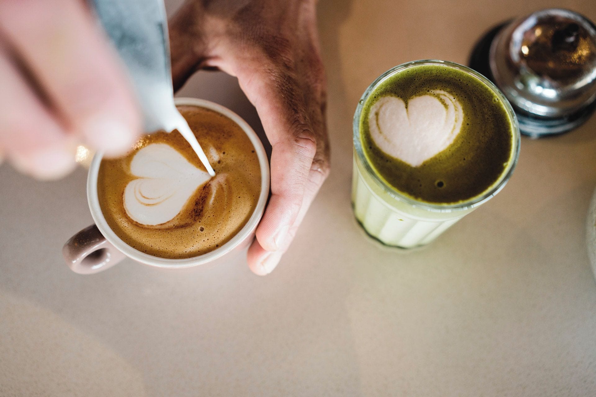 A hand holding a cup of coffee with a heart-shaped latte art on the surface.