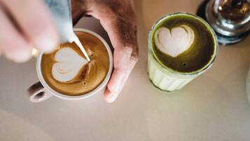A hand holding a cup of coffee with a heart-shaped latte art on the surface.
