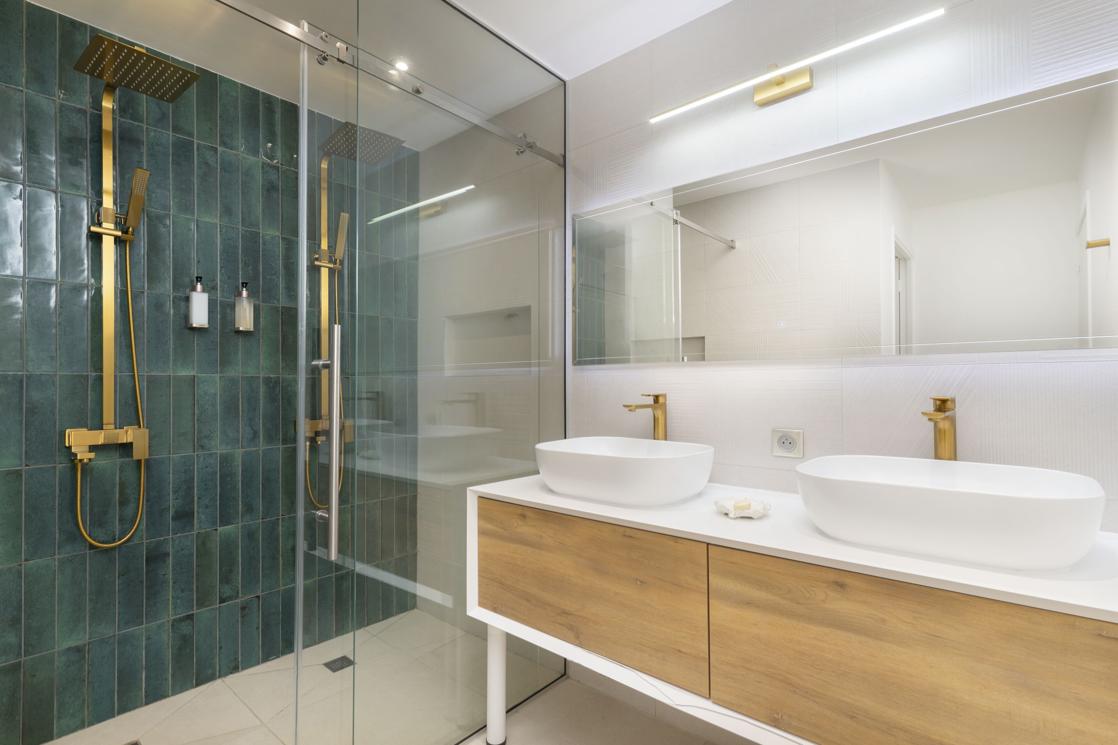A modern bathroom with a glass-enclosed shower, two sinks with gold faucets, and a wooden vanity.