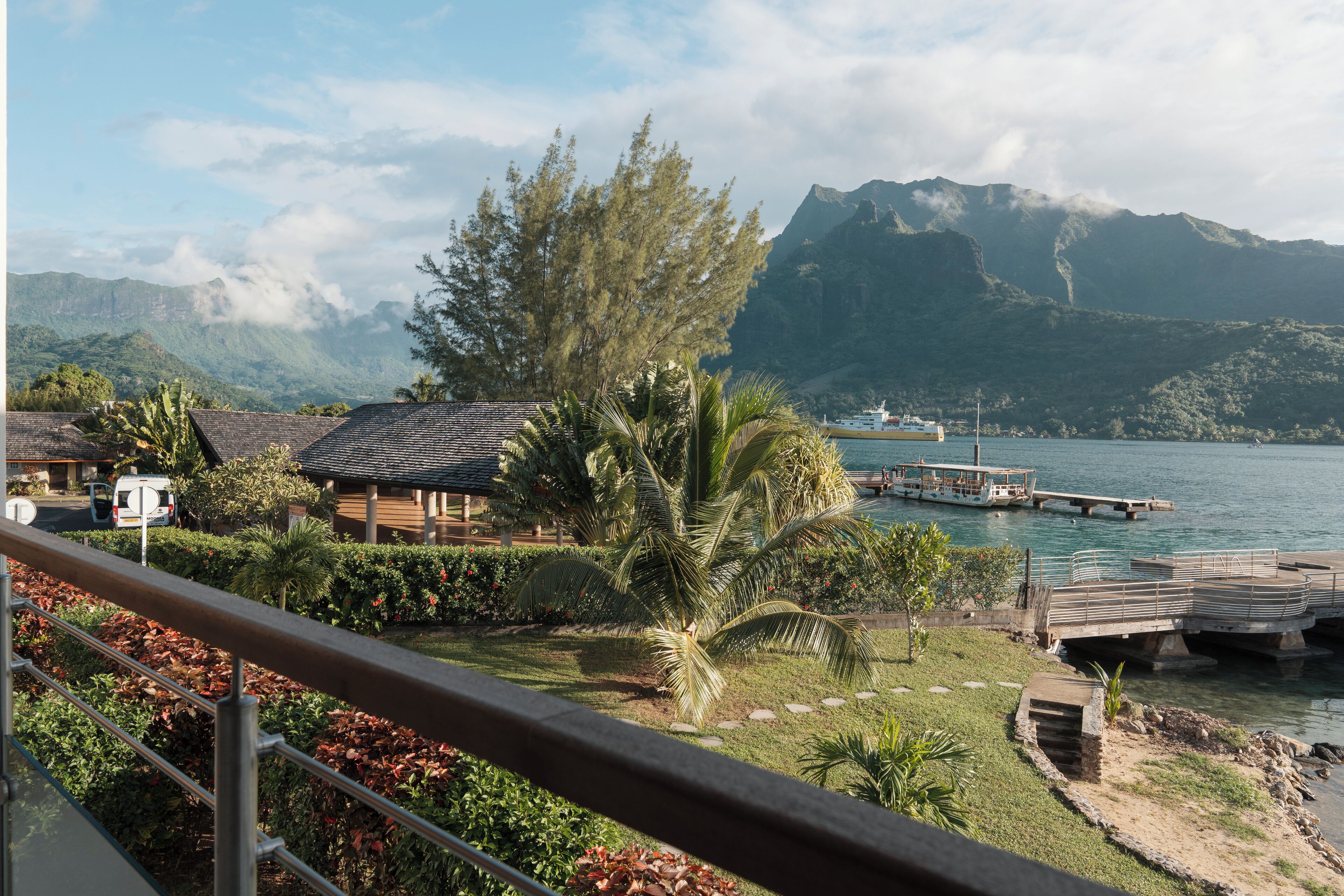 A coastal view with a wooden house, palm trees, and a dock extending into the water.