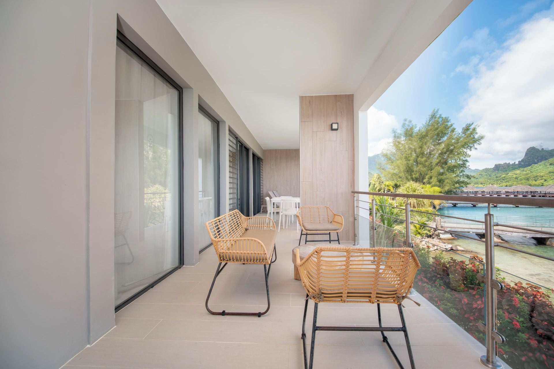 Un balcón con sillones de mimbre, una mesa y vistas a una masa de agua y vegetación.