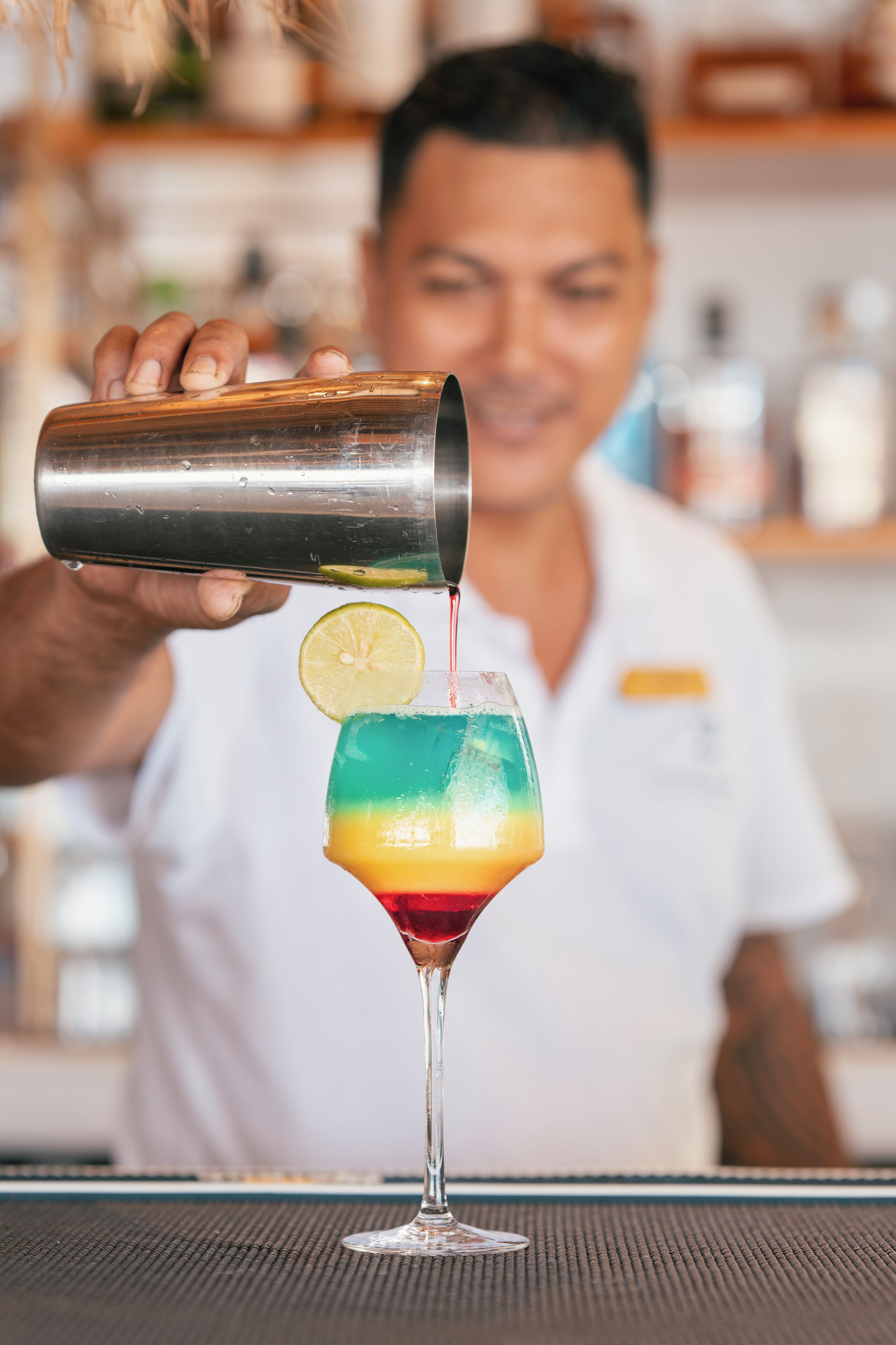 Un barman verse une boisson dans un verre, en y ajoutant une tranche de citron vert.